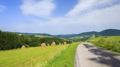 Grüner Feldweg führt durch eine hügelige Landschaft mit Heuballen.