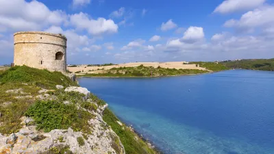 Historischer Wachturm an der Küste von Menorca mit Blick auf das türkisfarbene Meer.