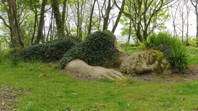 Skulptur einer Hand ragt aus dem grünen Rasen der Lost Gardens of Heligan.