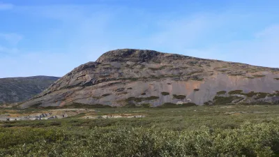 Grönländische Landschaft mit felsigem Hügel und grüner Vegetation.