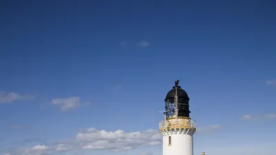 Weißer Leuchtturm steht auf einer grünen Klippe mit Blick auf das Meer.