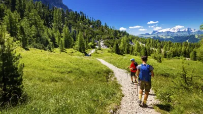 Zwei Wanderer gehen auf einem Pfad durch eine grüne Berglandschaft.