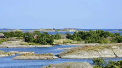 Rotes Haus inmitten der norwegischen Schärenlandschaft mit Felsen und blauem Wasser.