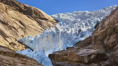 Blauer Gletscher zwischen hohen, braunen Felswänden in Norwegen.