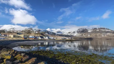 Islandische Häuser spiegeln sich im Wasser mit schneebedeckten Bergen im Hintergrund