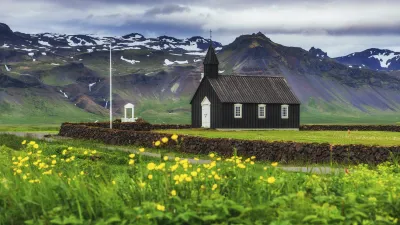Schwarze Holzkirche in Island mit gelben Blumen im Vordergrund