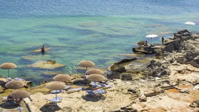 Sonnenliegen und Strohdächer an der felsigen Küste von Kalithea.