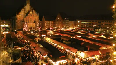 Belebter Weihnachtsmarkt mit mittelalterlicher Architektur im Hintergrund.