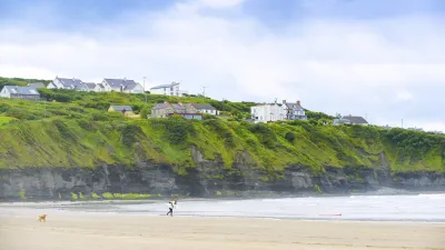 Strandlandschaft mit Häusern auf einem grünen Hügel am Meer.