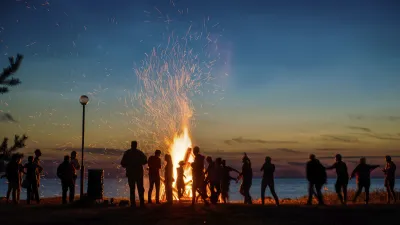 Menschen feiern am Lagerfeuer am Strand bei Sonnenuntergang.
