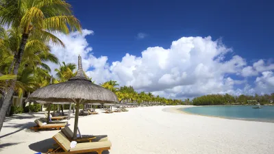 Sonnenliegen und Palmen säumen den weißen Sandstrand am türkisfarbenen Meer.