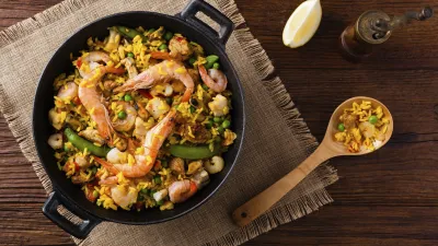 Köstliche Paella mit Garnelen und Gemüse in einer schwarzen Pfanne.