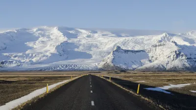 Schneebedeckte Berge säumen eine lange Landstraße in Island.