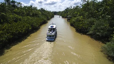 Ein Schiff fährt auf einem Fluss zwischen üppiger Vegetation.