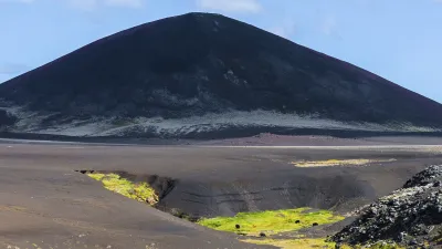 Lavafeld mit grünem Moos und einem kegelförmigen Berg im Hintergrund