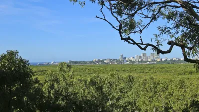 Blick über grünes Buschland auf die Skyline von Darwin unter einem blauen Himmel.