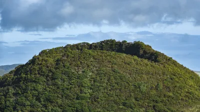 Grüner Vulkankrater mit dichter Vegetation unter bewölktem Himmel.