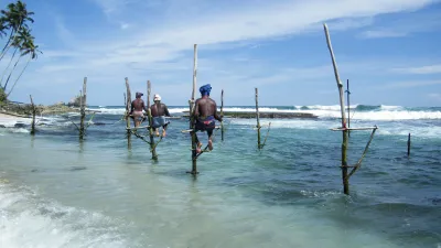 Fischer sitzen auf Stelzen im türkisfarbenen Meer in Sri Lanka.