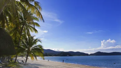 Palmengesäumter Strand mit Blick auf das blaue Meer und Berge.