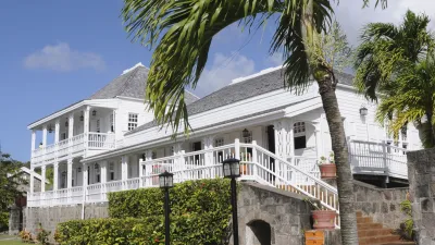 Weißes Herrenhaus mit gepflegtem Garten und Palmen.