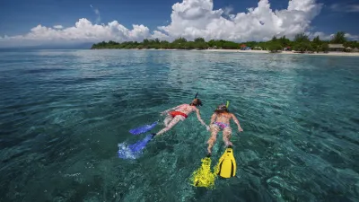 Zwei Schnorchler erkunden das türkisfarbene Wasser vor einer tropischen Insel.