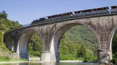 Dampfzug fährt über eine historische Steinbrücke über einen Fluss.