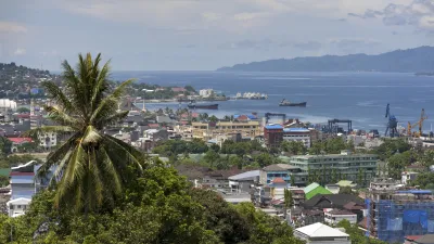Bunte Häuser und Schiffe liegen vor grüner Hügellandschaft.