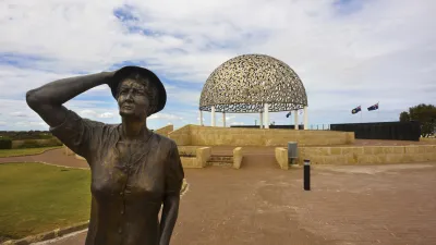 Frau mit Hut blickt auf Denkmal am Meer.