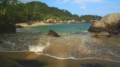 Wellen brechen an einem sandigen Strand mit Felsen im Tayrona Nationalpark.
