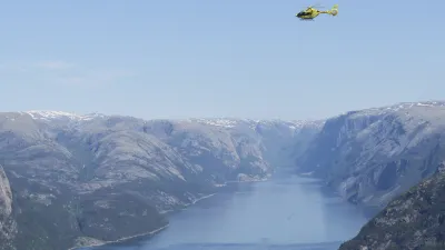 Helikopter fliegt über dem norwegischen Lysefjord mit steilen Felswänden.
