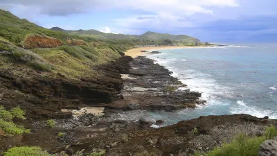 Felsige Küstenlinie mit Wellen und üppiger Vegetation an einem sonnigen Tag.