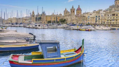 Buntes Fischerboot im Hafen von Malta mit Stadtkulisse im Hintergrund