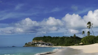 Weitläufiger Strand mit Palmen und Blick auf eine grüne Halbinsel.