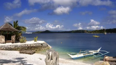 Ein traditionelles Boot liegt am weißen Sandstrand vor türkisfarbenem Wasser.