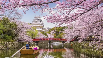 Ein Boot fährt auf einem Kanal vor dem Himeji-Schloss unter blühenden Kirschbäumen.