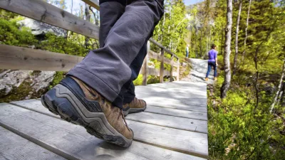 Wanderer geht auf einem Holzsteg durch eine grüne Landschaft