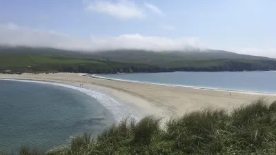 Weitläufiger Sandstrand mit sanften Dünen und blauem Meer.