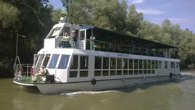 Weißes Passagierschiff fährt auf einem Fluss mit Bäumen am Ufer.