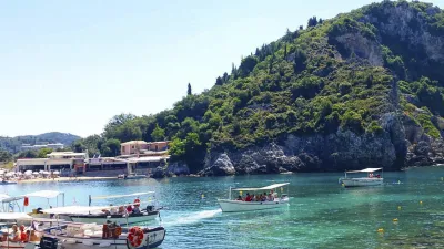 Boote liegen im türkisfarbenen Wasser vor einer grünen Küstenlandschaft.
