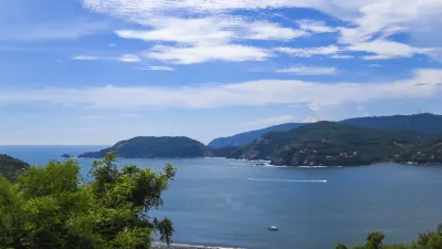 Panoramablick auf eine Küstenbucht mit grünen Hügeln und blauem Himmel.