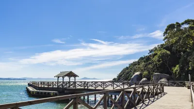 Holzsteg führt ins blaue Meer mit üppiger Vegetation am Ufer