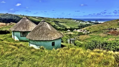 Traditionelle Xhosa-Hütten stehen in einer grünen Landschaft Südafrikas.
