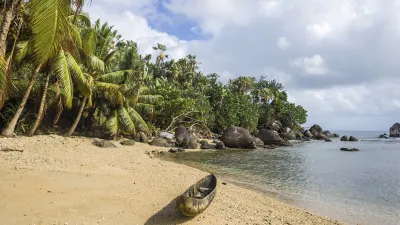 Ein kleines Boot liegt an einem tropischen Strand mit Palmen und Felsen.