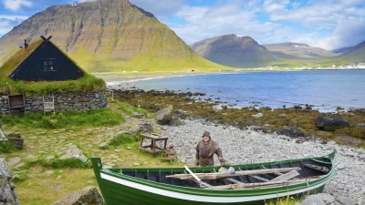 Ein Fischer steht neben einem grünen Boot vor einer traditionellen Hütte.