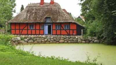 Traditionelles rotes Fachwerkhaus mit Strohdach am Teich.