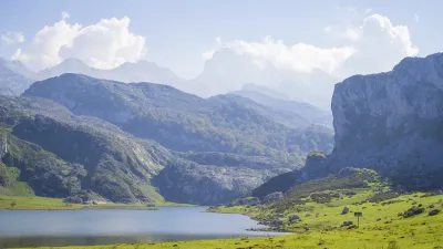 Bergsee in grüner Landschaft mit bewölktem Himmel.