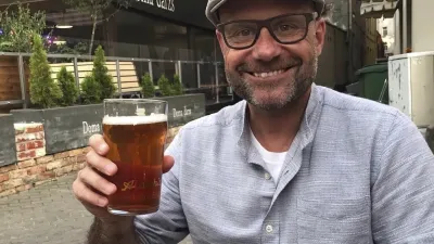 Ein lächelnder Mann hält ein Glas Bier im Freien.
