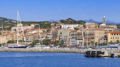 Korsischer Hafen mit bunten Häusern und Segelbooten im Wasser.