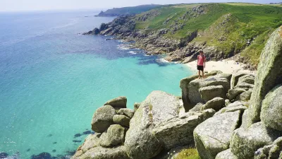 Frau steht auf Felsen und blickt auf die Küstenlandschaft.