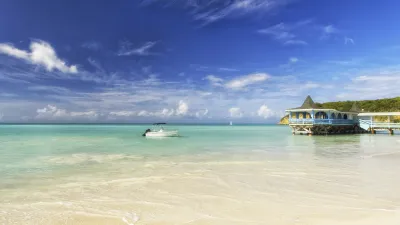 Türkisblaues Wasser umspült einen weißen Sandstrand mit einem kleinen Haus.